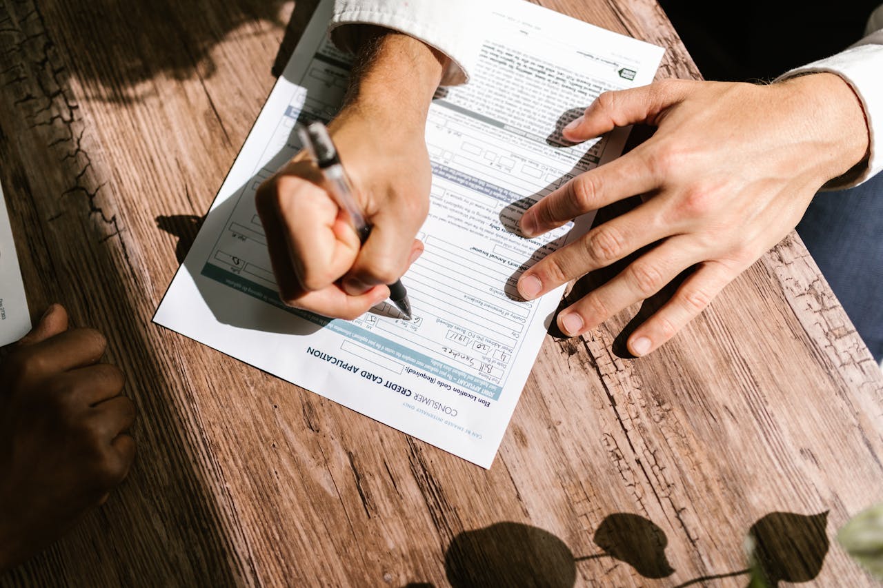 Hands writing on a consumer loan credit application form on a wooden table.